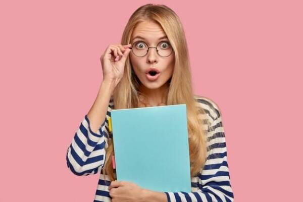 colegiala-pelo-claro-sorprendida-expresion-estupefacta-mantiene-mano-borde-gafas-ve-algo-increible_273609-17830